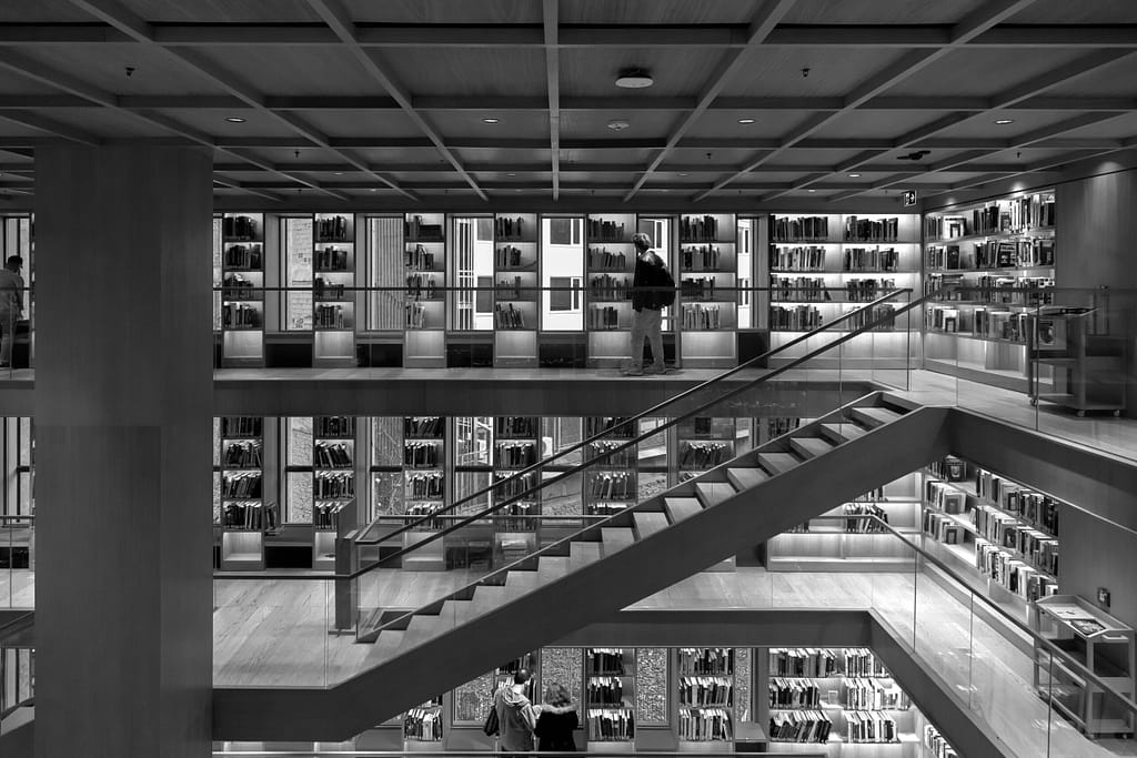 Black and white photo of a modern library interior with visible bookshelves and wooden stairs.